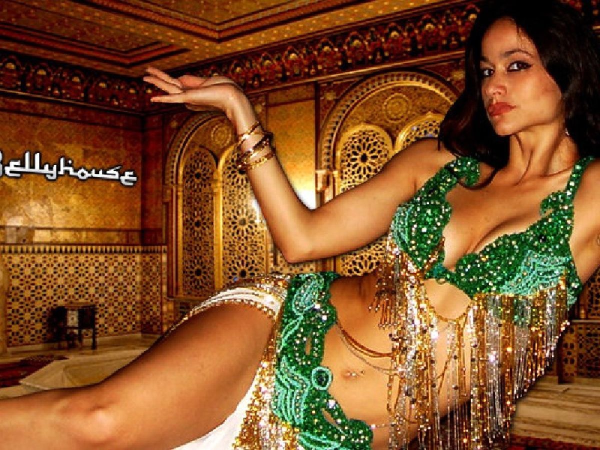 Bellyhouse picture created from famous music producer Bellyhouse, with Anandi from Bellydance Marbella, Woman with black hair laying sideways with belly dance costume with green emeralds shinning beeds and golden beeds and she is tanned red lipstick and white skirts she is serious mystical face posing with her hand up such as holding a vase. Egyptian style pose.
